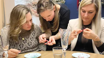 Three women making jewelry at table.
