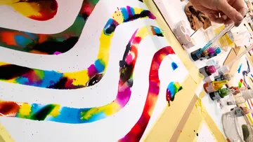 Bunte Farbwellen auf Papier, Hand mit Pipette.