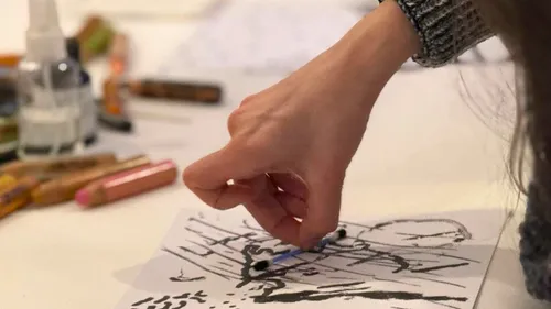 Hand drawing on paper with art supplies nearby.