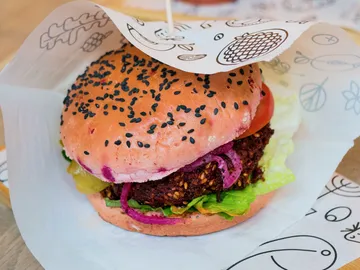 Burger mit buntem Brötchen, Salat und Zutaten, präsentiert in Papier.