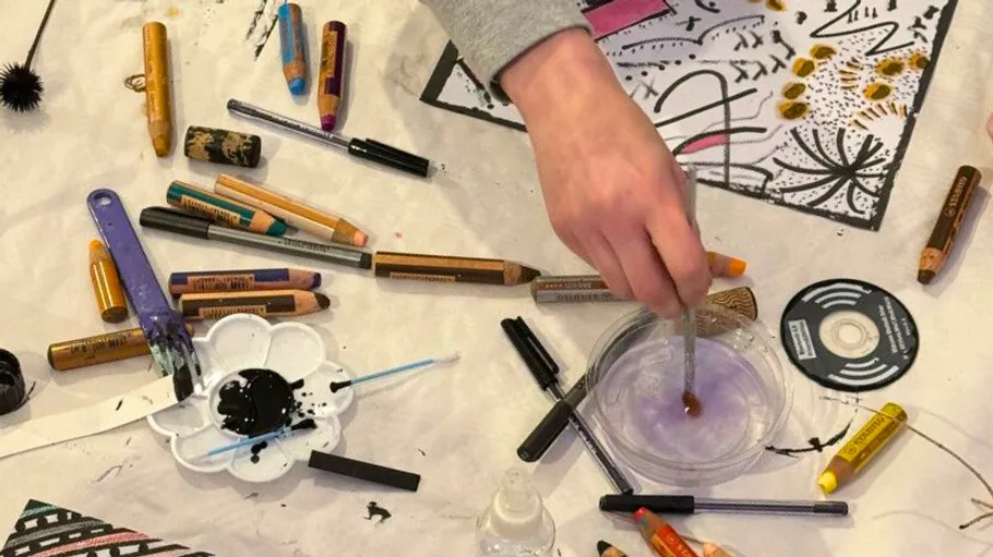Artist's hand painting on cluttered desk.