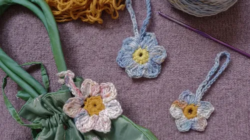 Crocheted flowers beside green bag on purple fabric.
