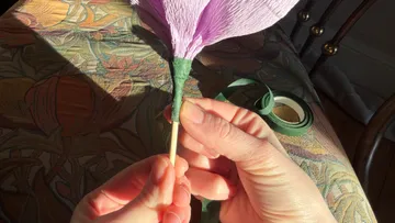 Hands wrapping purple paper flower on stem.