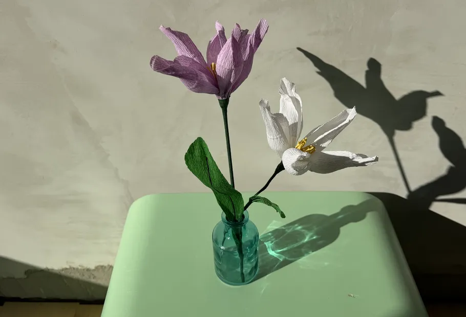 Papierblumen in Glasvase auf Tisch.