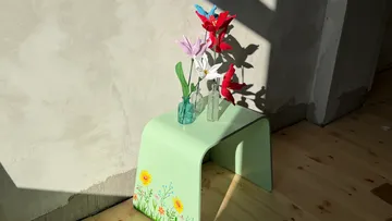 Colorful paper flowers on painted green bench.