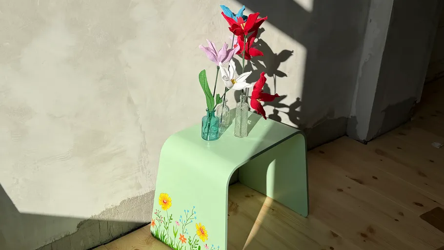 Bunte Papierblumen auf bemalter grüner Bank.