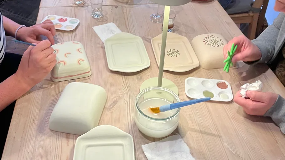 Adults decorating ceramic plates at a table.