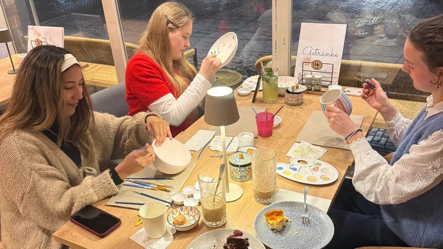Three women painting pottery at a table.