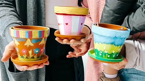Hands holding colorful painted flower pots.