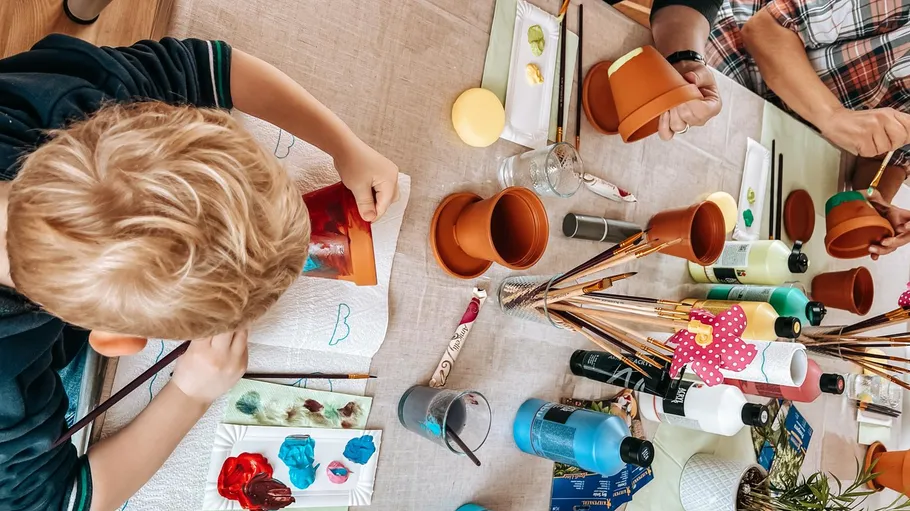 Children painting flower pots at a table.