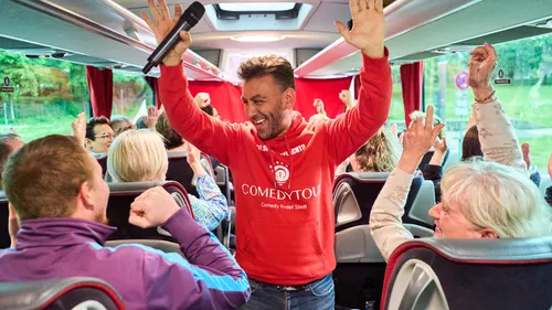 Komiker unterhält Buspassagiere mit Mikrofon.