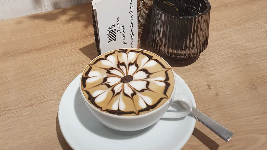 Kaffeetasse mit Latte Art auf Holztisch.