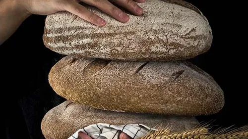 Hände stapeln Brote vor schwarzem Hintergrund.