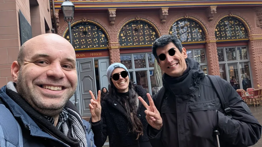 Three people smiling, making peace signs, outside building.