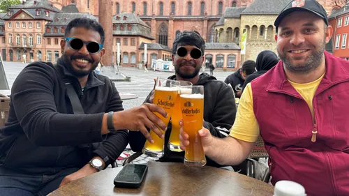 Three people holding beer glasses at outdoor table.
