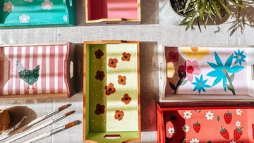 Bemalte Tabletts mit Blumen- und Tiermotiven auf Tisch.
