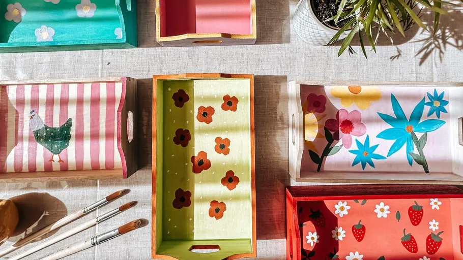 Painted trays with floral and animal designs on table.