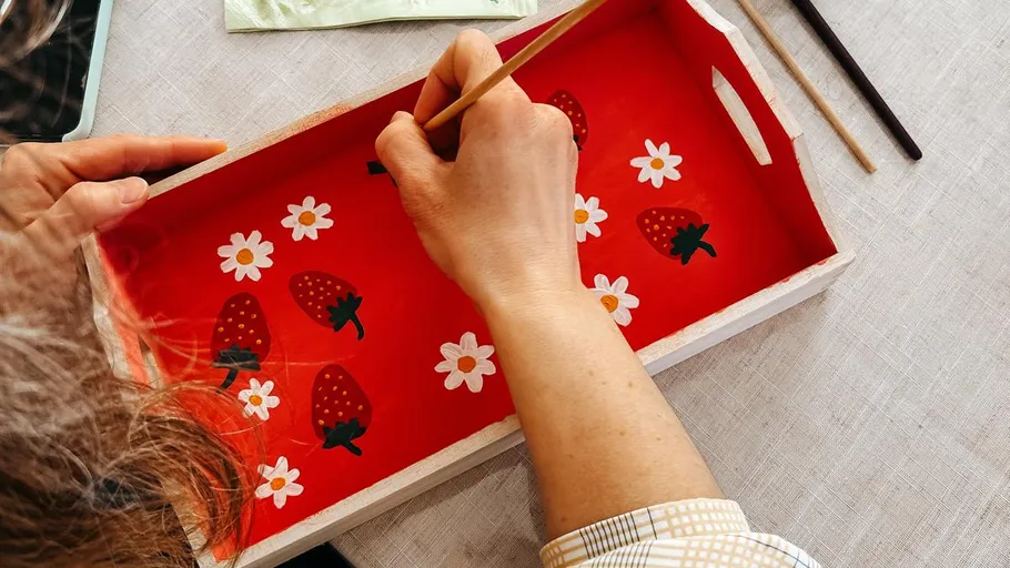 Person painting strawberries on a wooden tray.