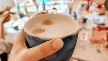 Hand hält Kaffeetasse in geschäftiger Umgebung.