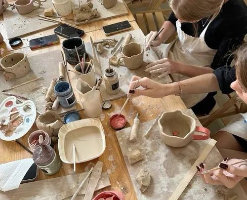 People painting ceramic mugs in art studio.