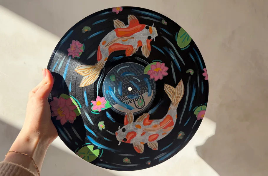 Hand holding painted vinyl record with koi design.