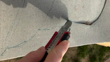 Hand schneidet Stoff mit Cuttermesser im Freien.