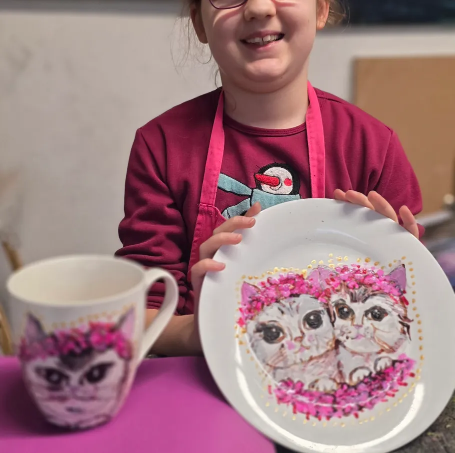 Mädchen hält Teller mit Katzengemälden.
