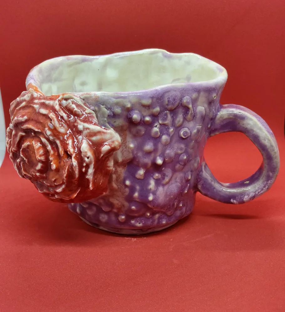 Lila Tasse mit rotem Blumendesign, roter Hintergrund.