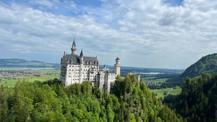 Schloss auf Hügel mit Wald, bewölkter Himmel.