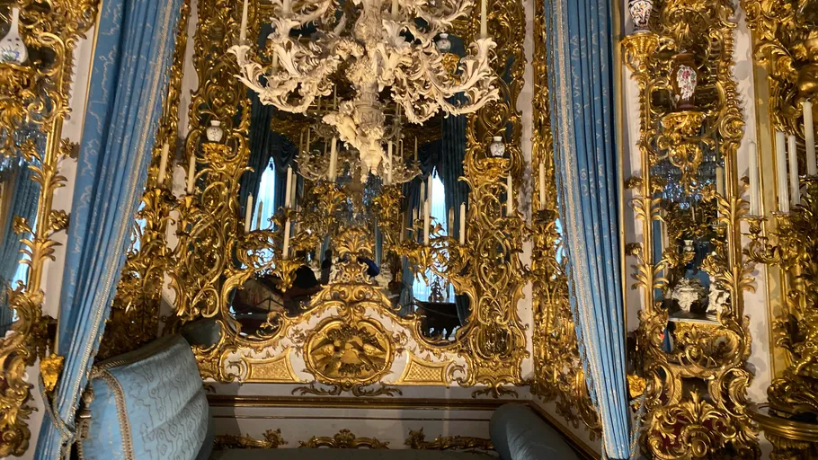 Ornate gold room with blue drapes, chandelier.