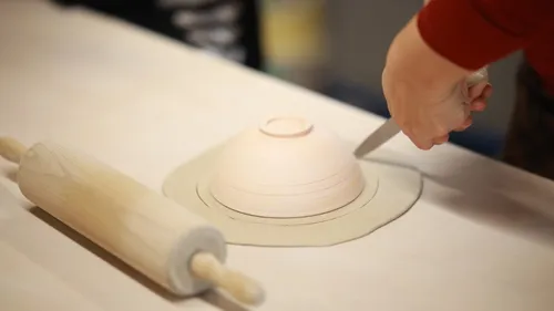 Person cutting dough around bowl on table.