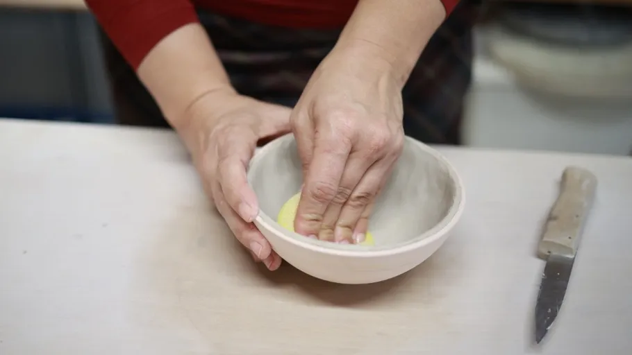Hands cleaning bowl with sponge, knife nearby.
