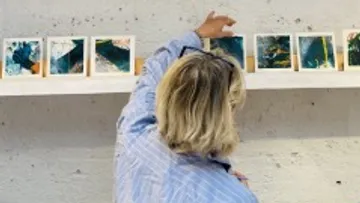 Person arranging artwork on a gallery wall.