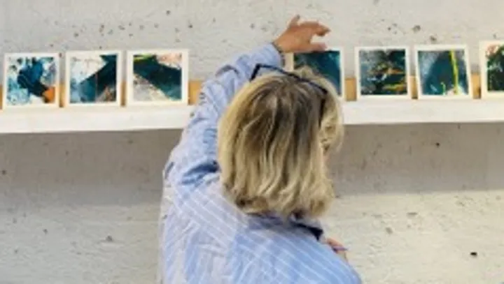 Person ordnet Kunstwerke an einer Galeriewand an.