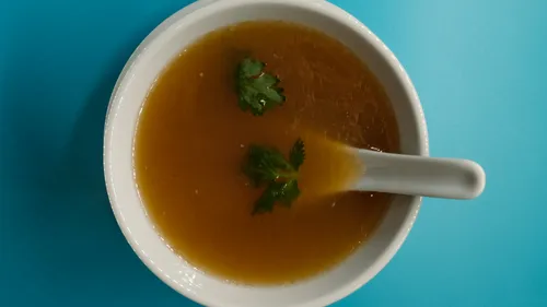 Soup with herbs in white bowl, blue background.