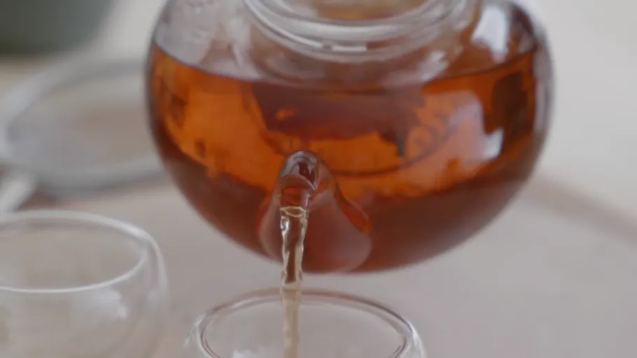 Teekanne gießt Tee in ein Glas.