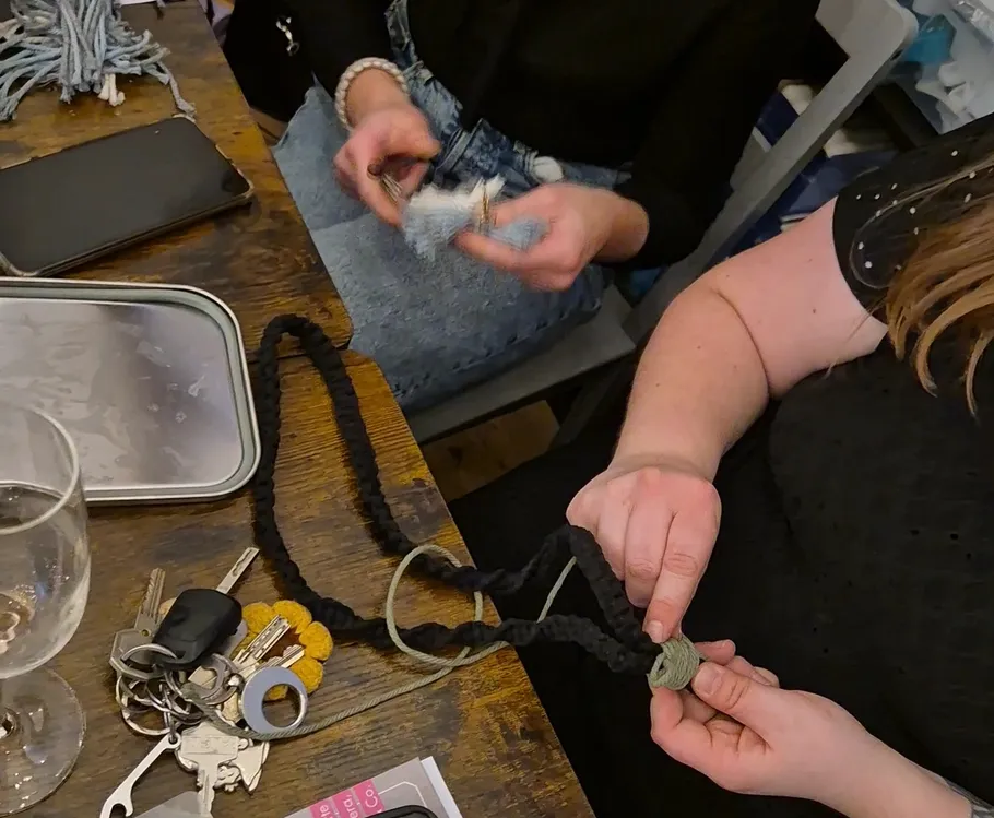 Two people knotting yarn at a table.