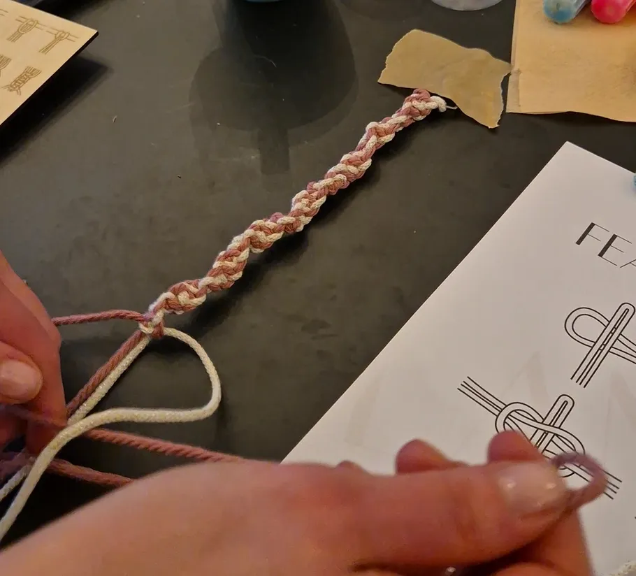 Hands braiding colorful cords on a table.
