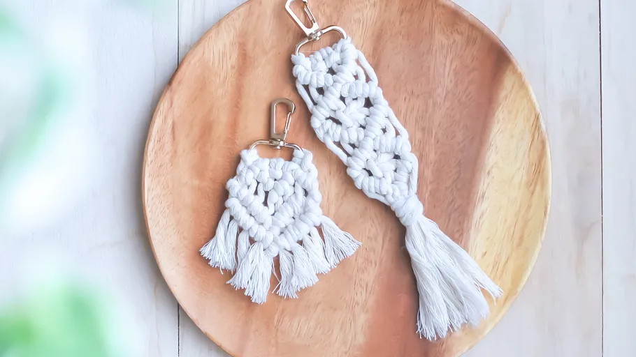 Two macramé keychains on a wooden plate.