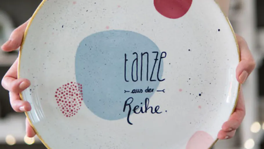 Hand holding plate with decorative text.