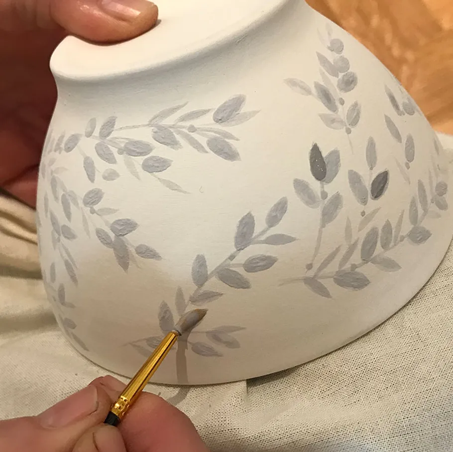 Person malt florales Design auf Keramikschale.