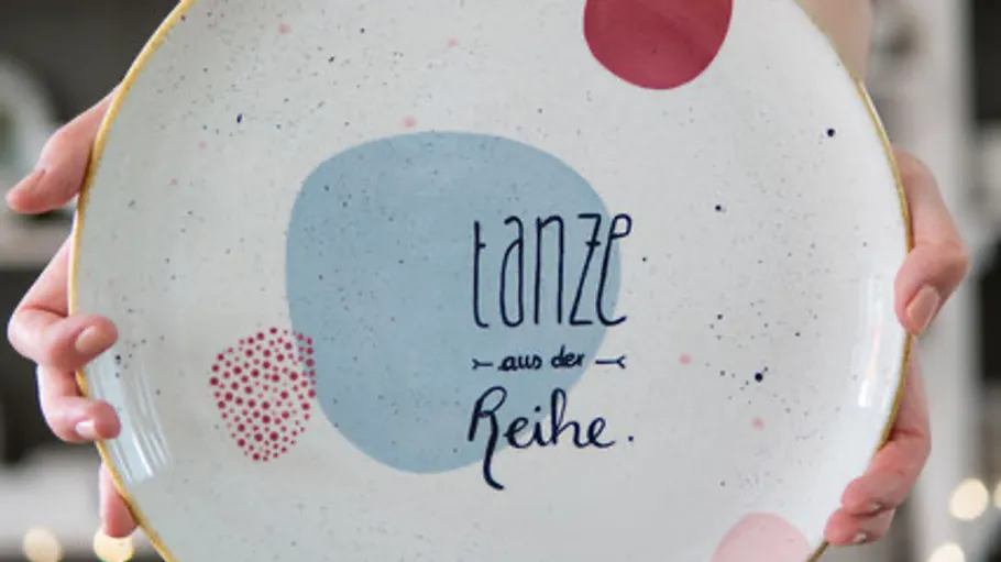 Decorative plate with colorful design held by hands.