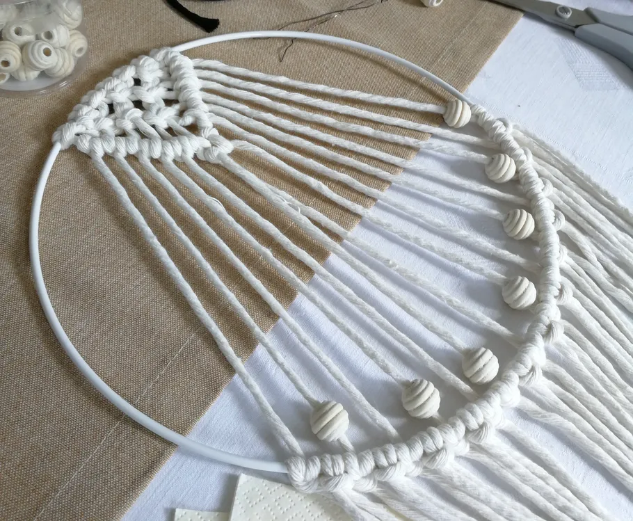 Macrame ring with threads and beads on table.