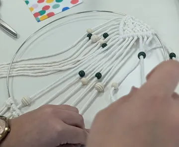 Hände fertigen ein Makramee-Design mit Perlen.