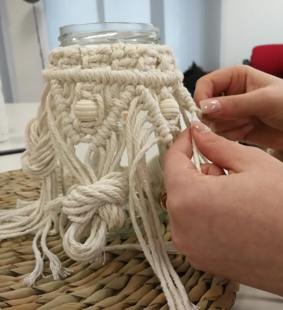 Hände machen Makramee an einem Glas.