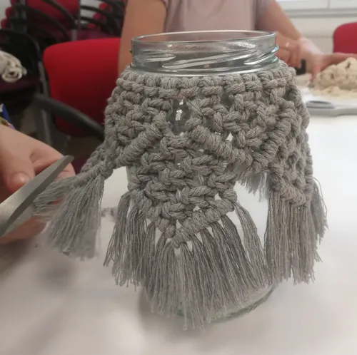 Einmachglas mit Makramee-Abdeckung auf Tisch.