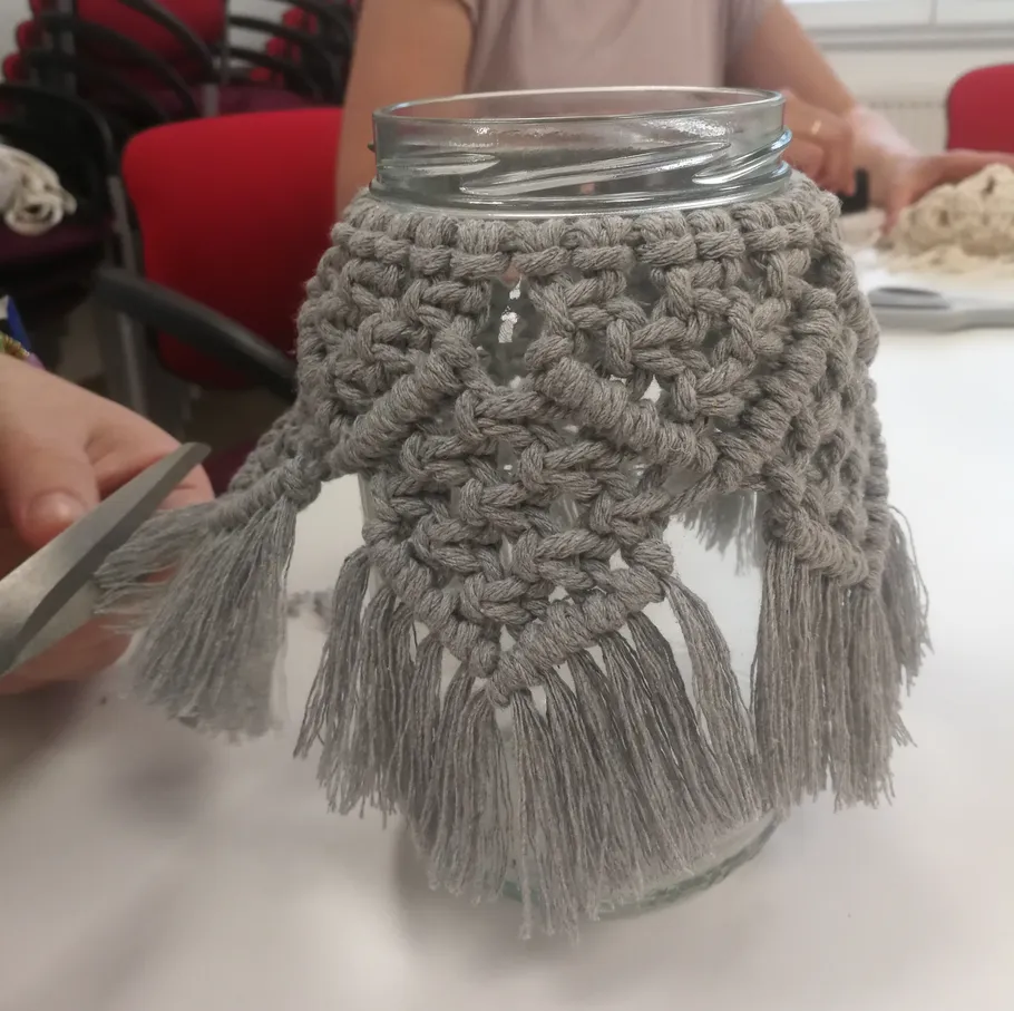 Einmachglas mit Makramee-Abdeckung auf Tisch.