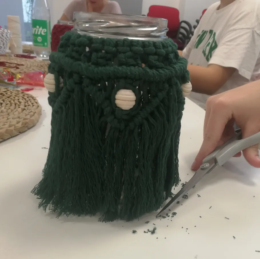 Hand trimming green macrame on glass jar.