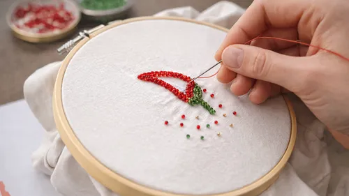 Hand stickt Perlen auf Stoff im Stickrahmen.