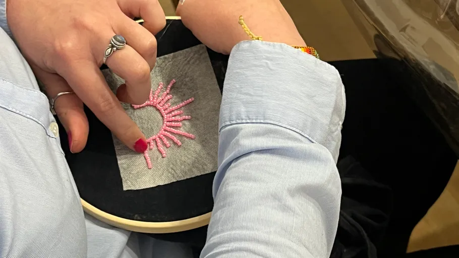 Person stickt rosa Design auf schwarzem Stoff.